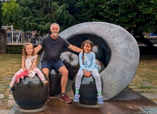Jonny and his granddaughters sitting on large bronze apples with a giant bronze hat behind